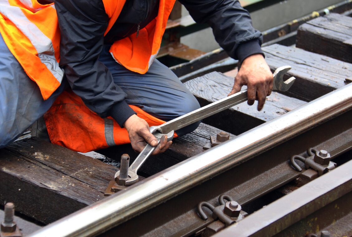 Worker tightening bolt on railway tracks.